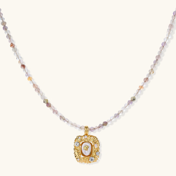 Ornate gold-plated pendant necklace with multicolored gemstone beads in purple, pink and clear tones on white background