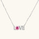 Sterling silver LOVE necklace with pink moissanite stone replacing the O, featuring crystal-set letters on delicate chain.