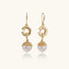 Gold sunburst charm earrings with baroque pearl drops on French hooks against cream background