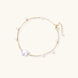 Delicate gold chain bracelet with baroque pearl centerpiece and small freshwater pearls on cream background.