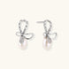 Silver bow-shaped stud earrings with baguette crystals and dangling white freshwater pearls on cream background