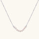 Delicate sterling silver chain necklace with small freshwater pearls arranged in a curved smile arc on cream background.