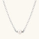 Dainty rhodium-plated silver chain necklace with centered 10mm freshwater pearl and crystal accents on cream background
