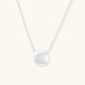Minimalist brushed sterling silver dome pendant on delicate chain against cream background, showing matte textured finish