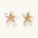 White enamel tropical flower earrings with sculptural gold-plated center and organic petal design on cream background
