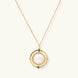 Gold pendant necklace with circular orbital design, iridescent mother-of-pearl center, and green zirconia accents