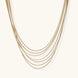 Seven delicate gold-plated snake chains create an elegant layered necklace on a neutral background.