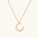 Gold crescent moon pendant with graduated white pearls on delicate chain against cream background