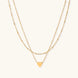Delicate double-chain gold necklace with tiny heart pendant on cream background