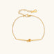 Delicate gold chain bracelet with minimalist bar and centered knot detail on cream background
