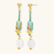 Gold-plated dangle earrings with turquoise threading, star charms, and white pearl beads against cream background.