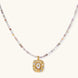 Ornate gold-plated pendant necklace with multicolored gemstone beads in purple, pink and clear tones on white background
