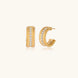 Textured gold huggie hoop earrings with raised ribbed rows creating dimensional sculptural design on cream background